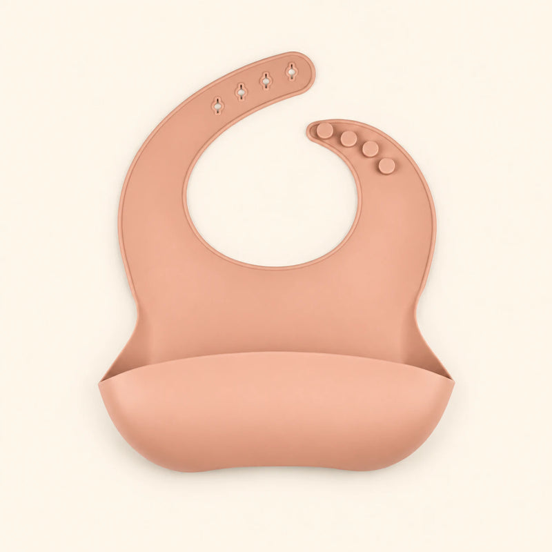 Peach silicone catch bib, with a scoop pocket and adjustable button-and-hole neck closure, on warm beige.