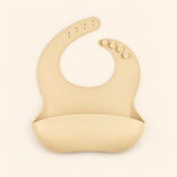 Oat Beige silicone catch bib, with a scoop pocket and adjustable button-and-hole neck closure, on warm beige.