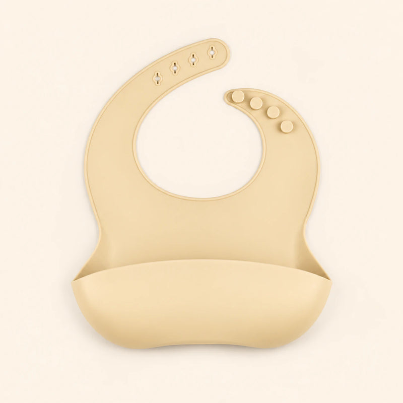 Oat Beige silicone catch bib, with a scoop pocket and adjustable button-and-hole neck closure, on warm beige.