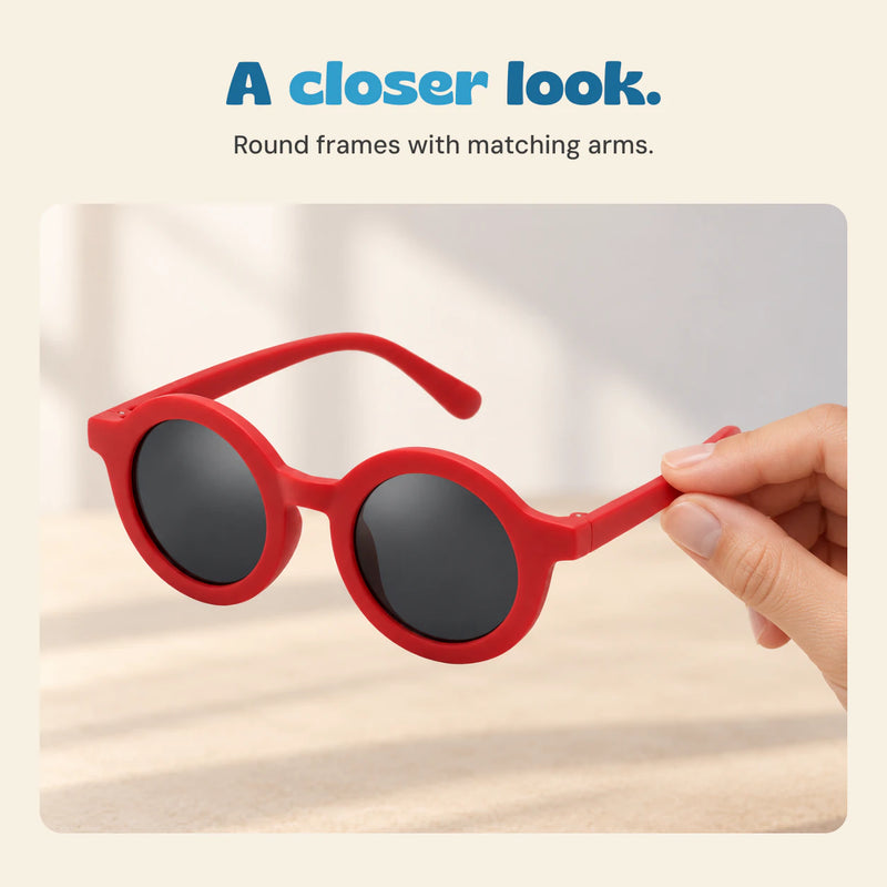 An adult hand holds the Cherry Red round sunglasses by one arm, showing the front frame and dark lenses.