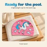 Pink unicorn swim cap resting on a folded towel beside a cream swim bag.