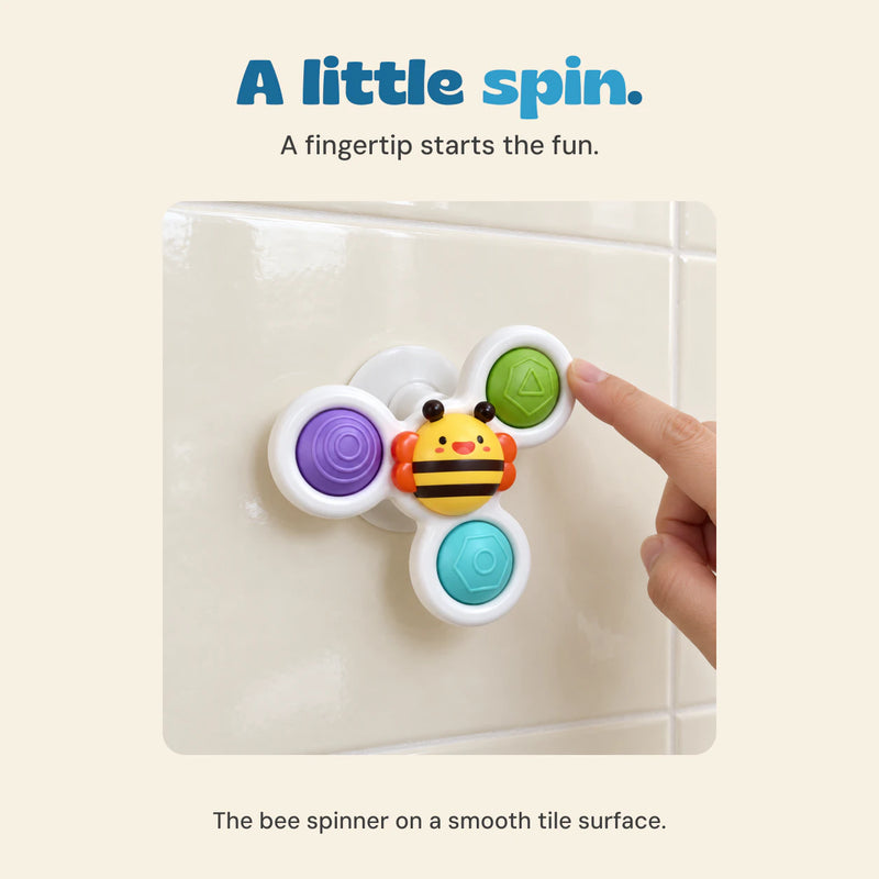 An adult fingertip touches the white rim of the bee spinner attached to a cream tile wall.