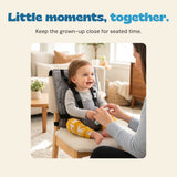 The existing child and adult sit together in the original home scene, with the actual Soft Grey chair harness visible.