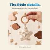 An adult hand steadies the wooden connector ring above the White mobile's complete cream crocheted star. Nearby wooden cloud shapes and cords are visible.
