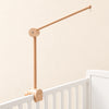 Natural wooden mobile arm with a round hinged joint, small hanging hook and clamp mounted on a white crib rail.