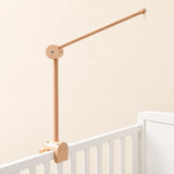 Natural wooden mobile arm with a round hinged joint, small hanging hook and clamp mounted on a white crib rail.