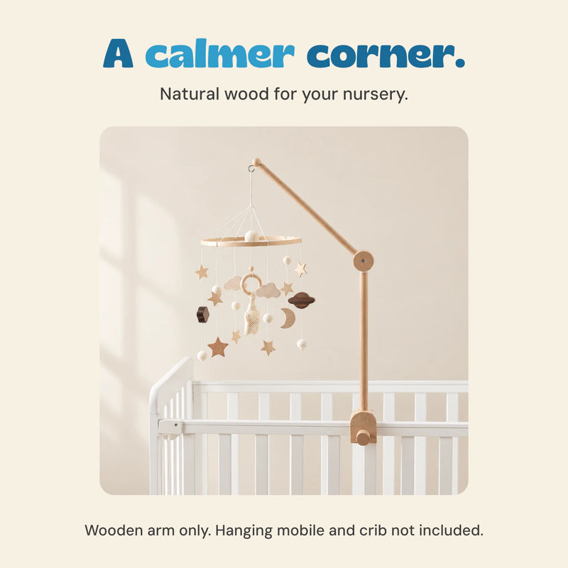 Wooden arm supports the original celestial mobile above an empty white crib in a calm neutral setting. The mobile and crib are not included.