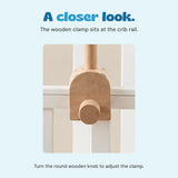 Close view of the wooden clamp and round adjustment knob where the mobile arm meets the crib rail.