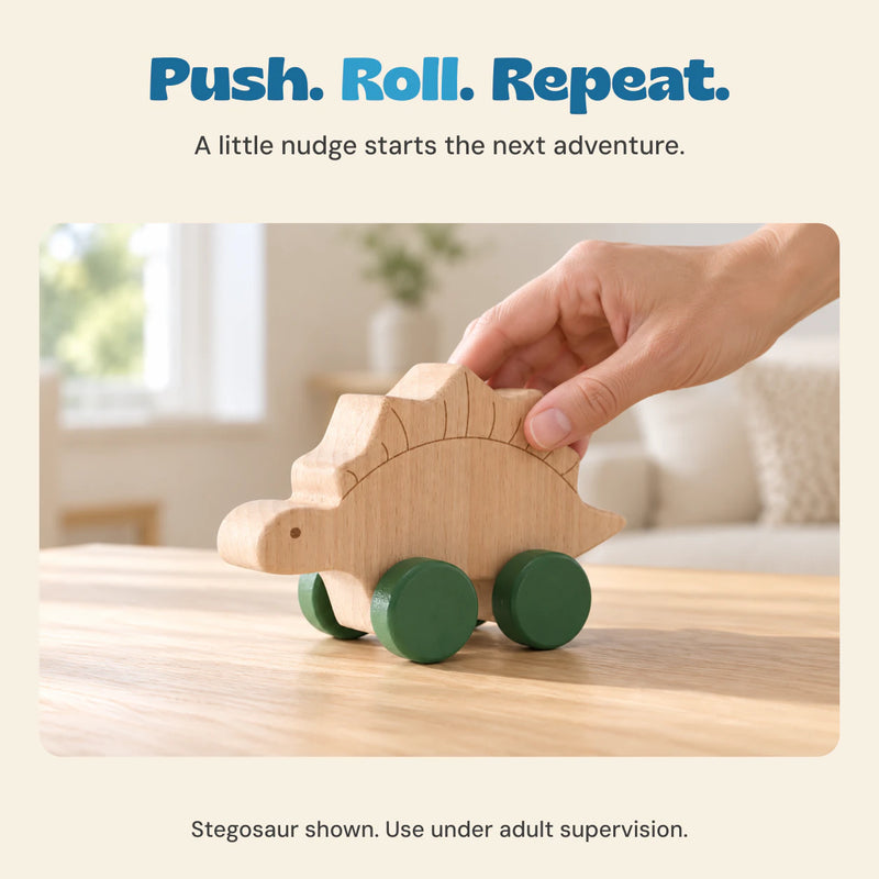 Adult hand gently pushes the wooden Stegosaur with green wheels on a pale oak tabletop.